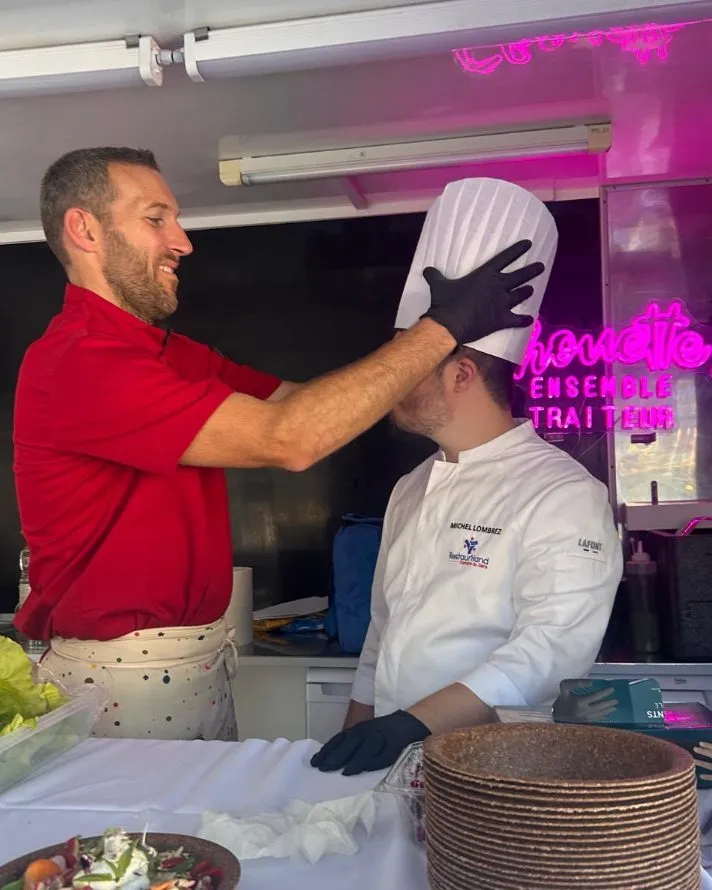 Dans le camion, un membre de l'équipe coiffe un jeune cuisinier de sa toque
