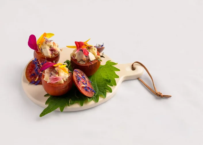 Bouchées garnies de fleurs comestibles, dressées sur une planchette ronde en bois