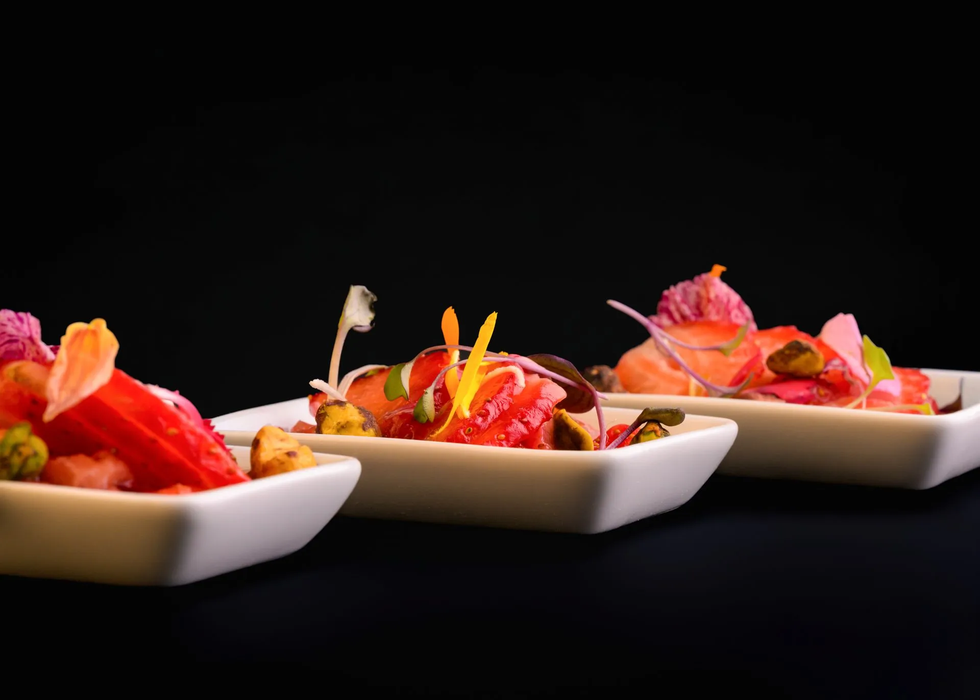 Trois coupelles dressées sur fond noir, produits de saison et fleurs comestibles