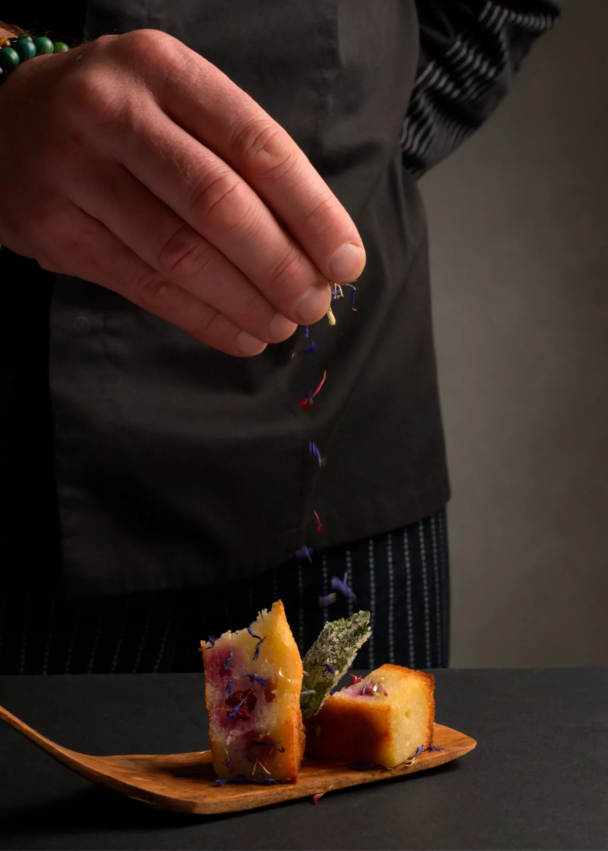 Le Chef parsème de fleurs comestibles une bouchée dressée sur une planchette de bois